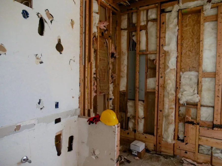 Damaged drywall and an opened wall with exposed wooden framing and insulation