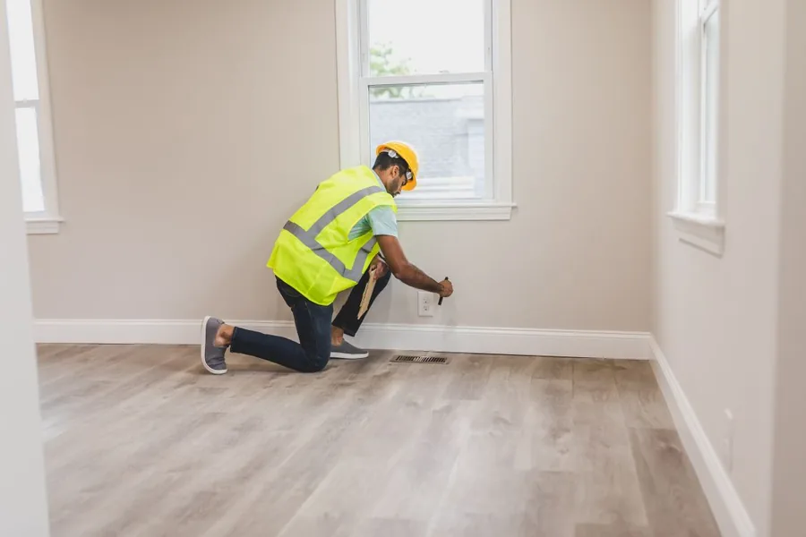 Home inspector in a high-visibility vest examining an electrical outlet in a room