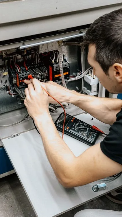 Electrician using a multimeter to test connections in an open electrical panel