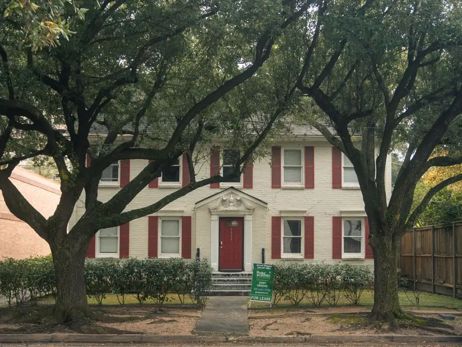 Classic Texas house shaded by large trees over the roofline